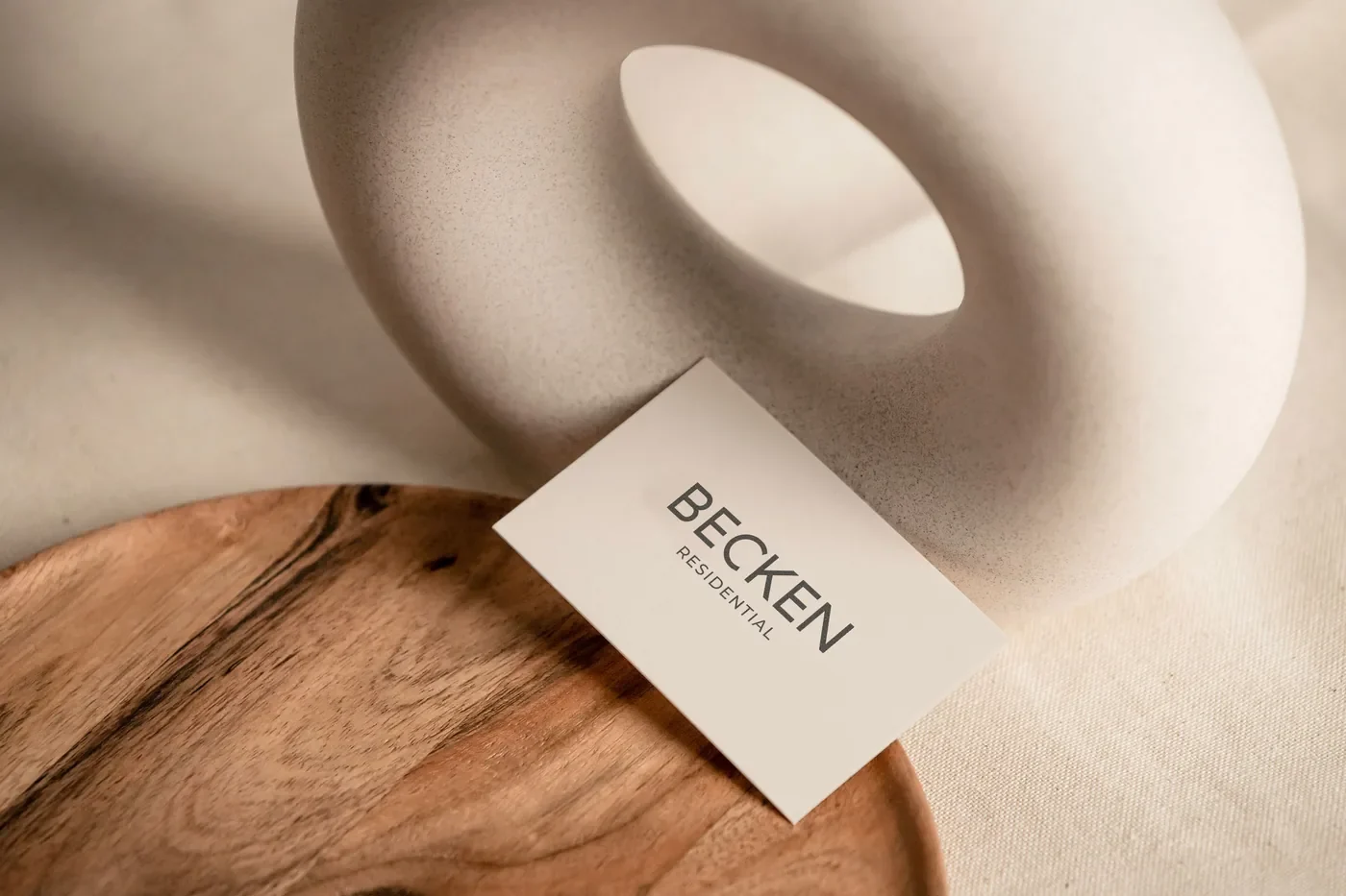 Visitenkarte von BECKEN Residential an einer hellen Keramikskulptur auf einem Holzteller