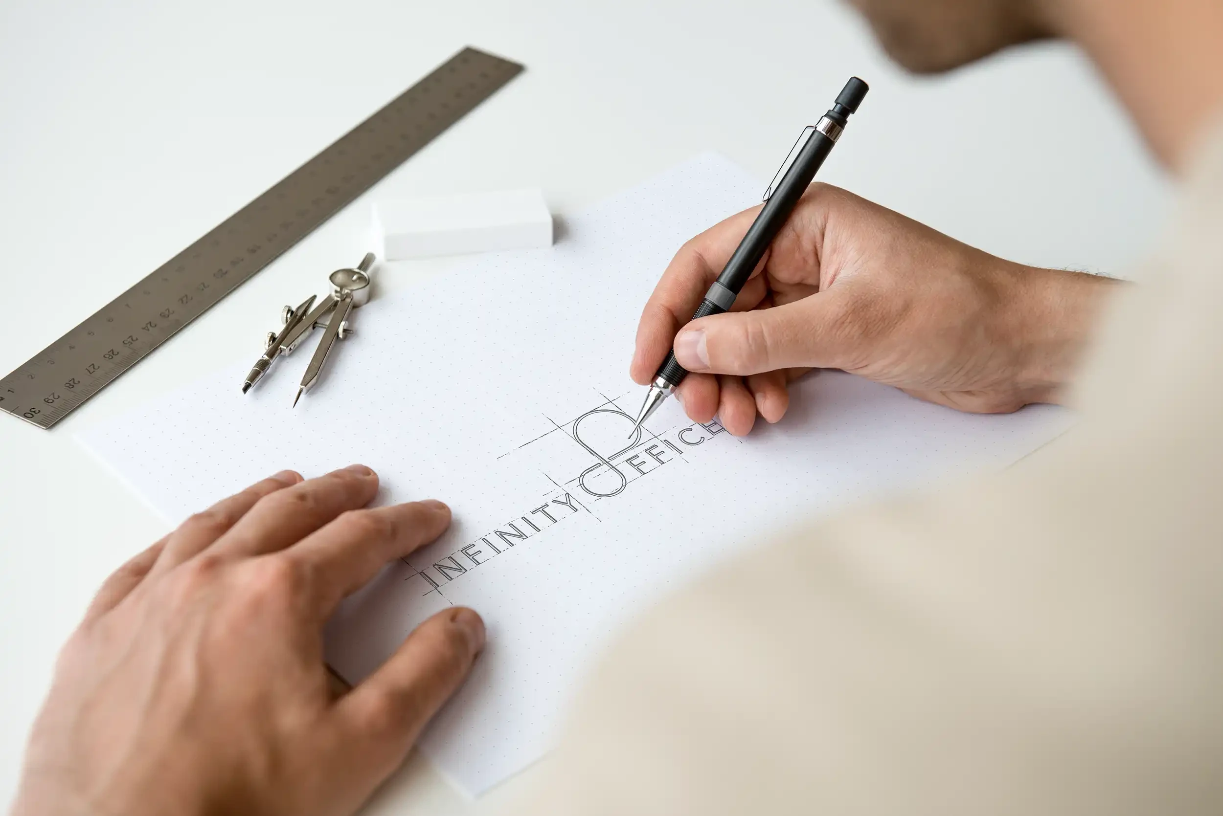 Hand zeichnet die Wortmarke Infinity Office mit Konstruktionslinien auf Punktpapier