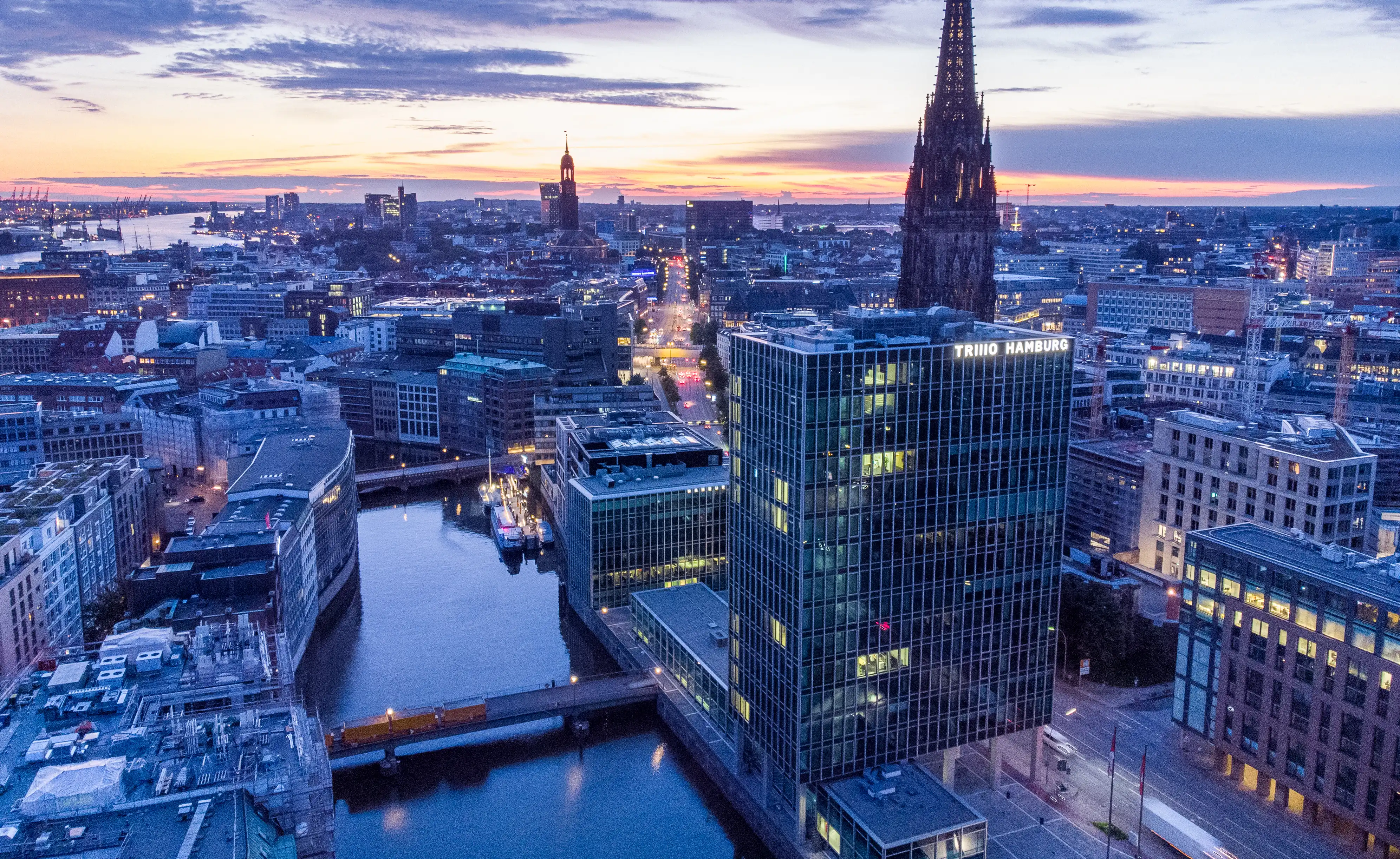 Luftbild des TRIIIO Hamburg im Abendlicht mit Kanal und Nikolaikirche